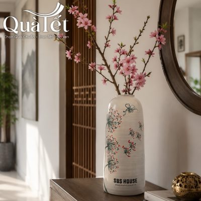 Chiếc bình gốm sứ vẽ tay bồ công anh mang thương hiệu SBS House cắm những cành hoa đào phai nở rộ đặt trang trọng trên kệ gỗ
