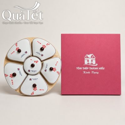 Bộ khay mứt dáng hoa vẽ đào đỏ kèm đế gỗ đặt cạnh hộp đựng màu đỏ in logo thương hiệu nổi bật