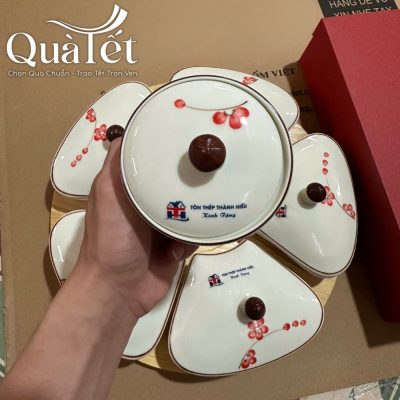 Cận cảnh nắp hũ tròn trung tâm của bộ khay mứt vẽ đào đỏ với logo in ấn chính xác