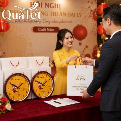 Đại diện doanh nghiệp mặc áo dài vàng trao túi quà tặng đồng hồ thiết kế riêng cho đối tác tại hội nghị tri ân cuối năm.